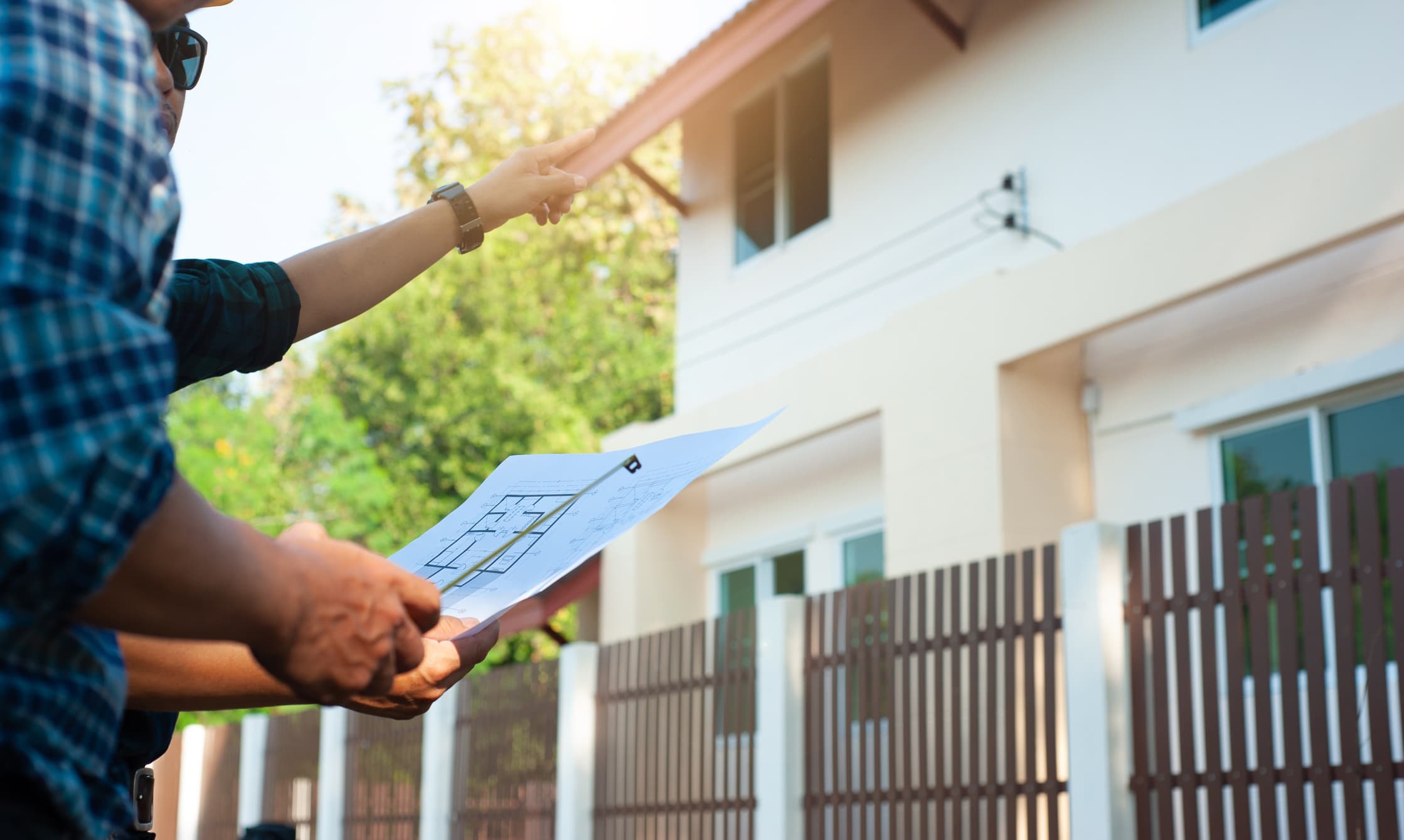 Roofing contractor reviewing home plans and pointing at a house during a roof inspection